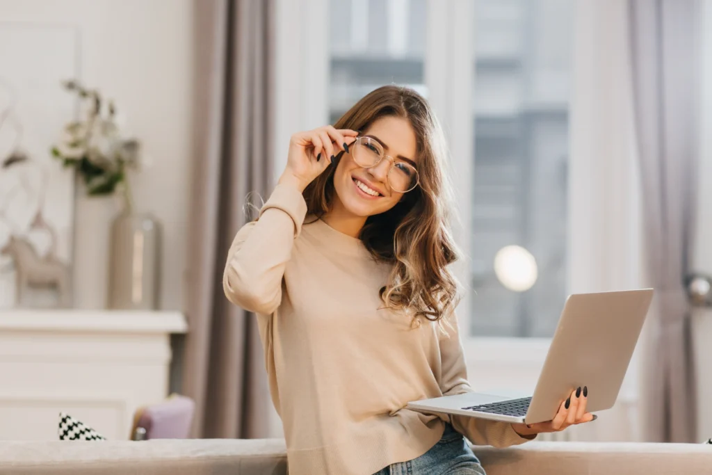 cute girl beige shirt touching glasses holding laptop with smile
