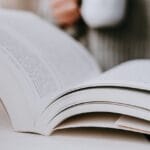 A person holding a cup of coffee while reading a book
